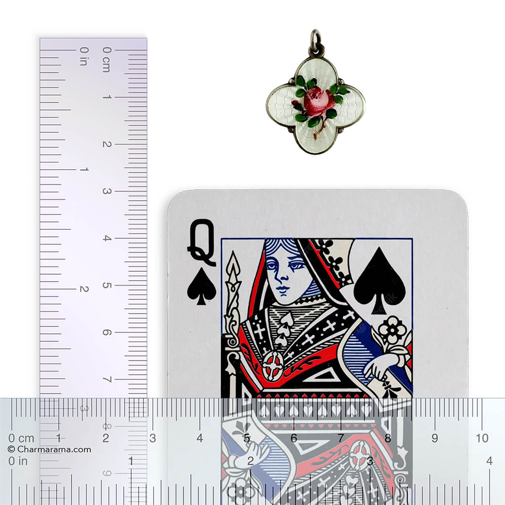 Pendant with floral design on a playing card next to a ruler for scale