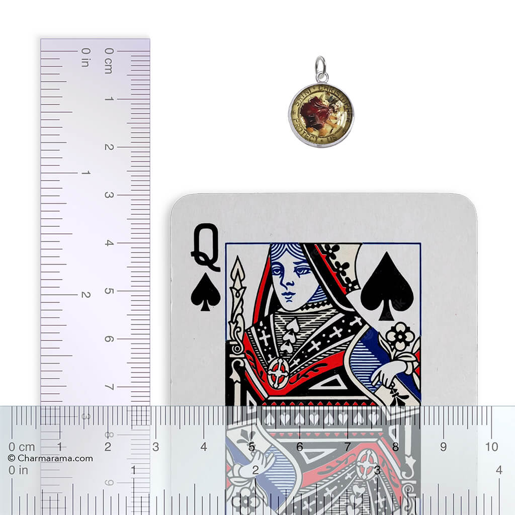 A vintage reverse crystal Saint Christopher charm with playing card and ruler for scale on a white background