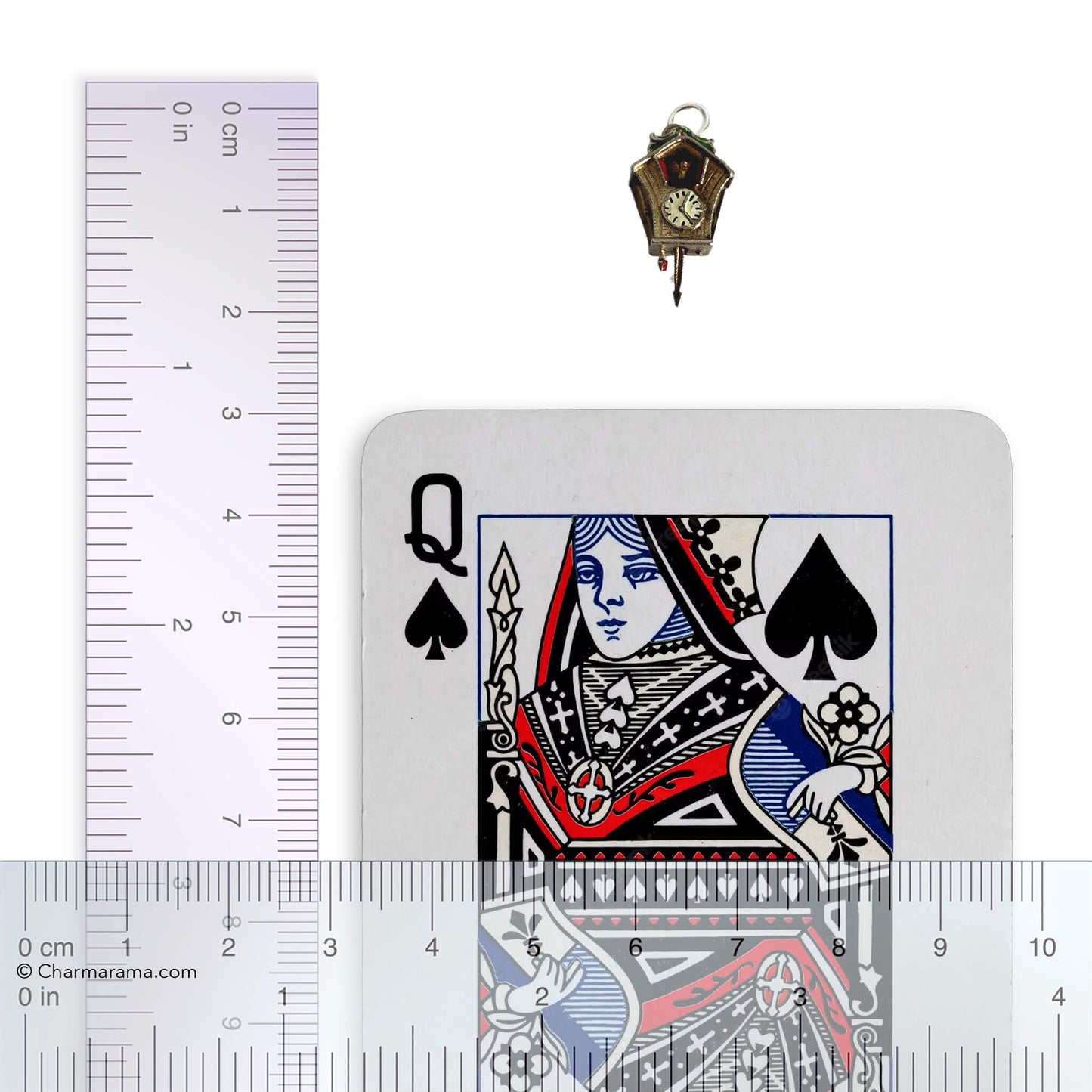 Cuckoo clock charm with playing card and ruler for scale on a white background