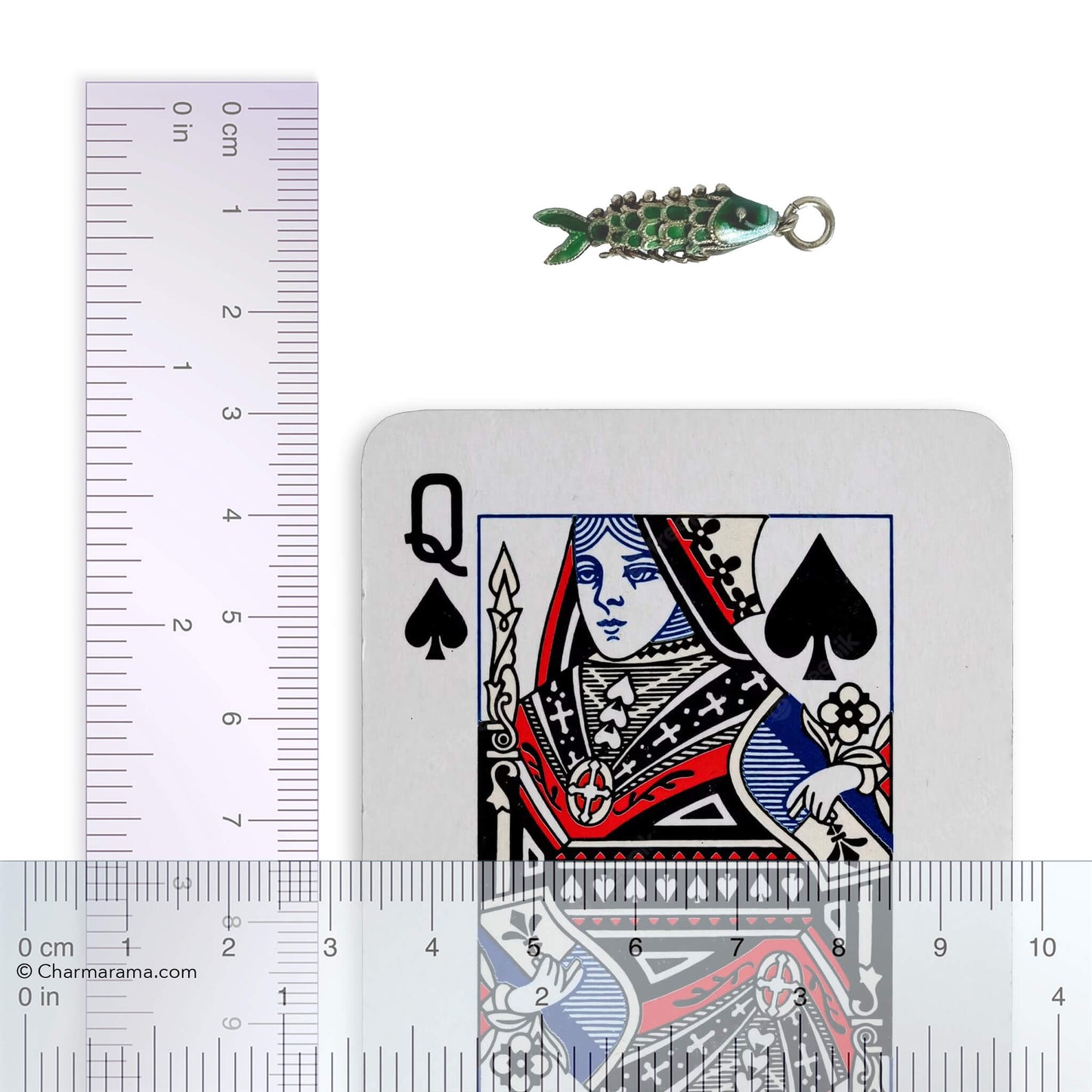 Vintage silver green enamel articulated fish charm with playing card and ruler for scale on a white background.