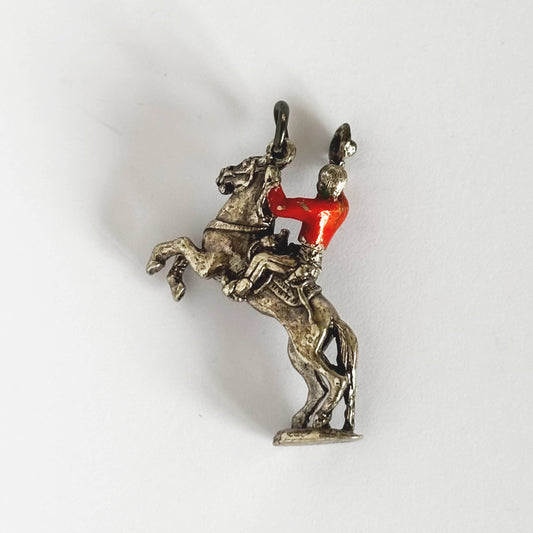 Cowboy on rearing horse silver charm with red enamel shirt on light grey background