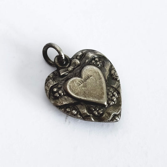 Silver heart-shaped pendant with intricate designs on a white background