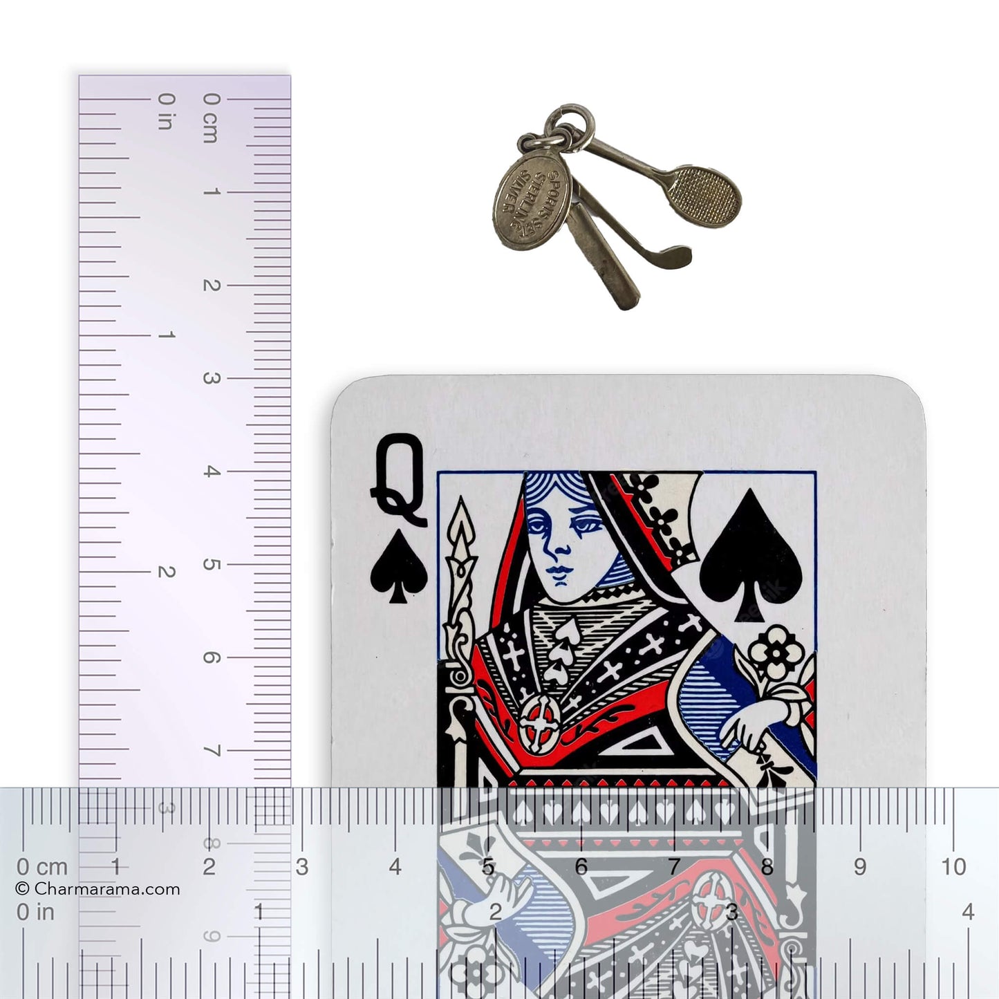 silver charm comprising a tennis racquet, golf club, cricket bat with a playing card and ruler for scale on a white background
