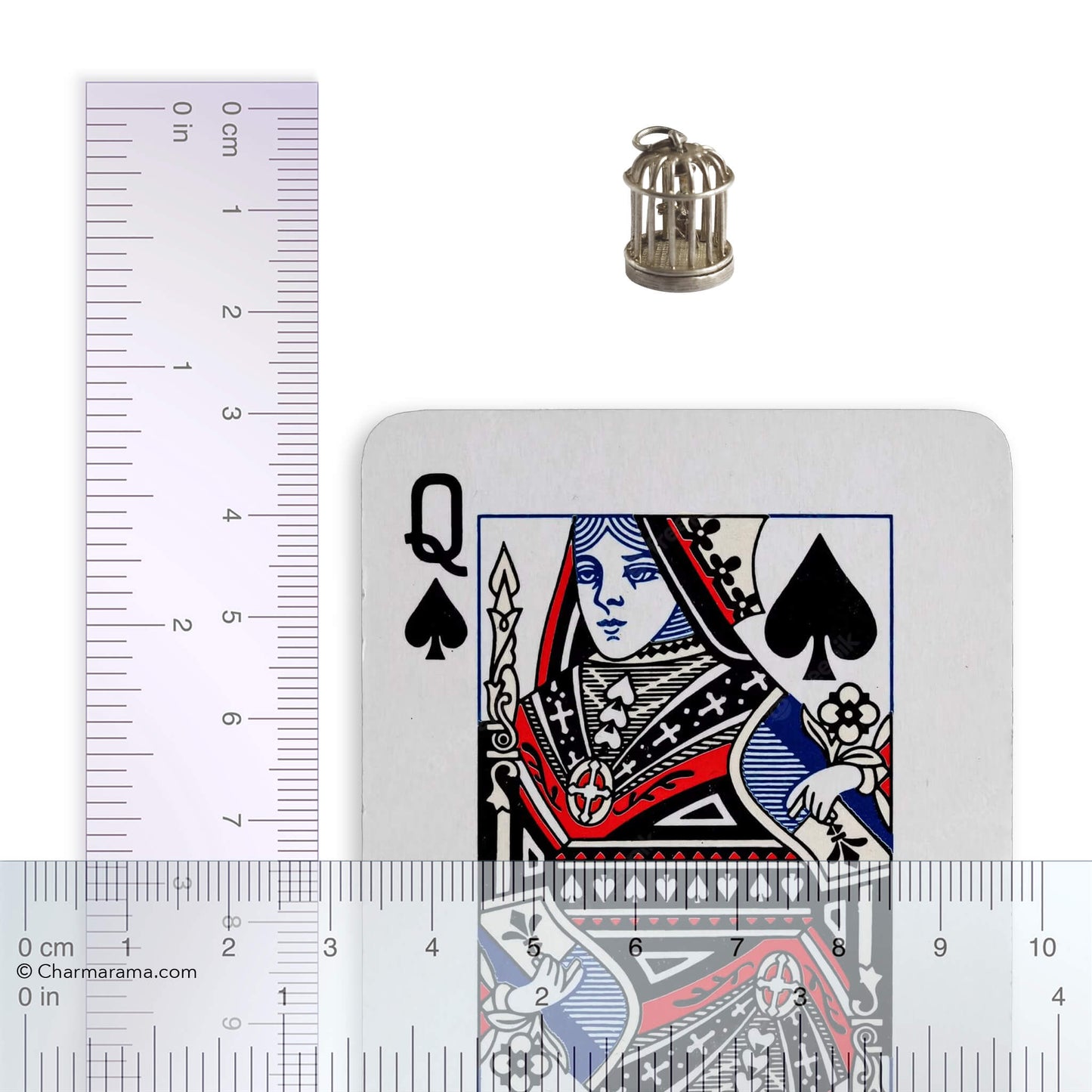 Vintage silver bird in a cage charm with playing card and ruler for scale on a white background.
