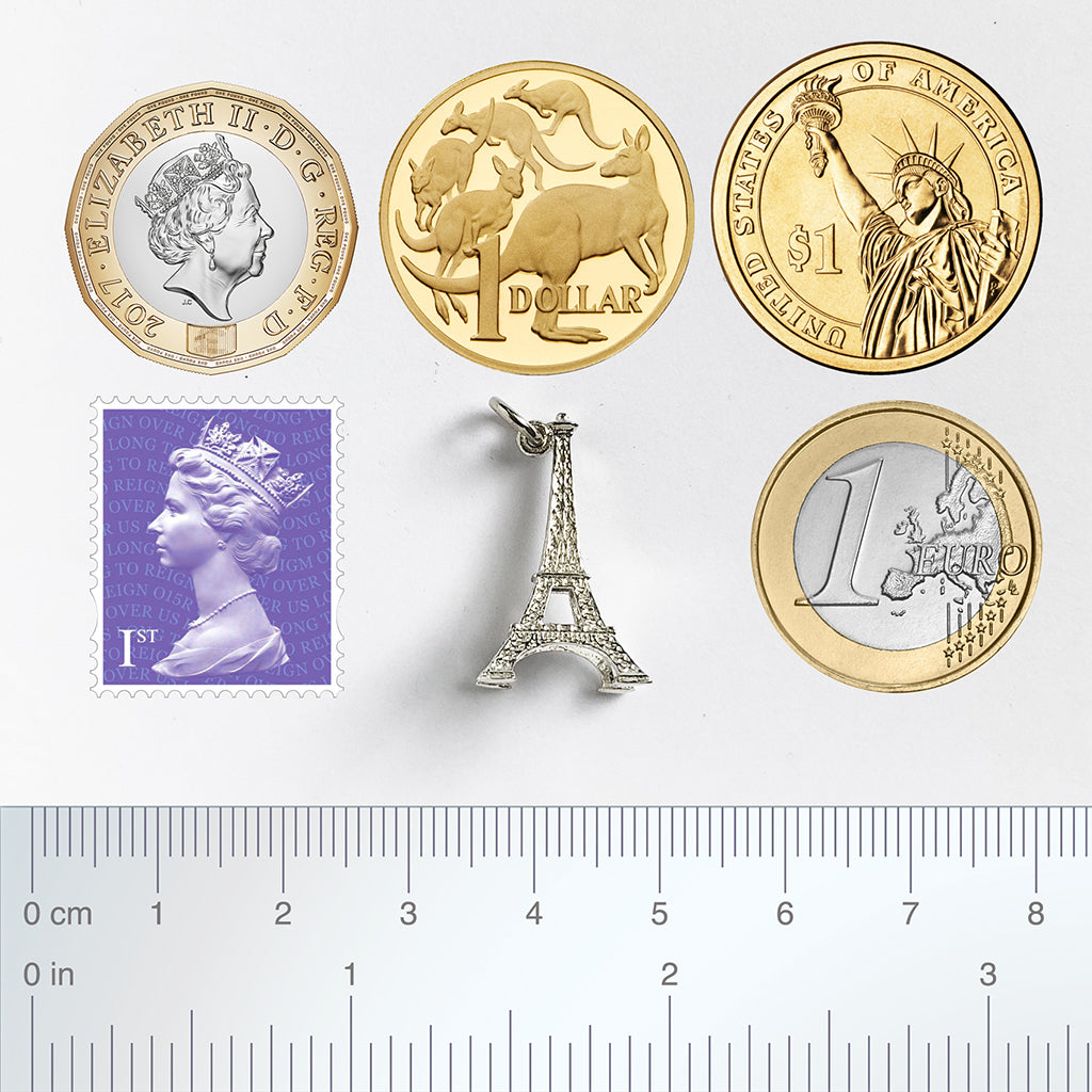 Sterling silver Eiffel Tower charm with coins postage stamp and ruler for scale on a white background