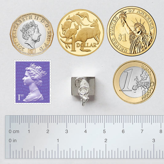 Sterling silver Australian dog on the tucker box charm viewed from above with coins, ruler and postage stamp for scale on a grey background