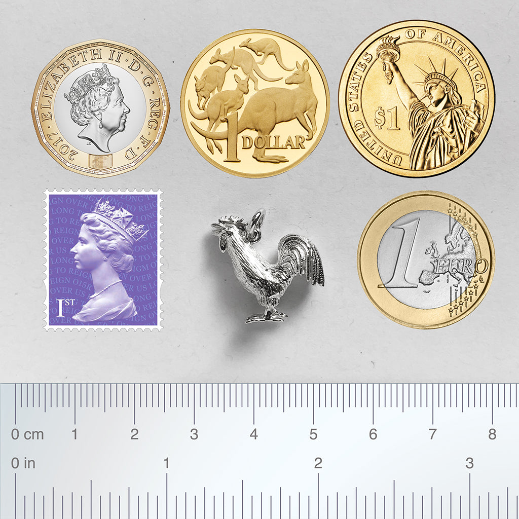 Sterling silver cockerel charm with coins stamp and ruler for scale on grey background