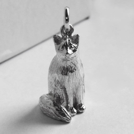 A sitting silver Birman cat charm on a grey background.