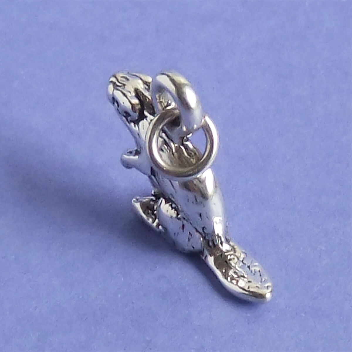 Sterling silver beaver charm pictured from above on a purple background