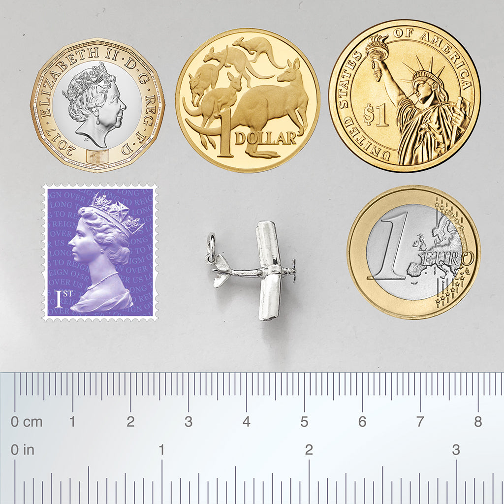 Silver biplane charm with coins, postage stamp and ruler for scale.