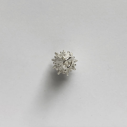 silver Christmas tree charm seen from above on a light grey background