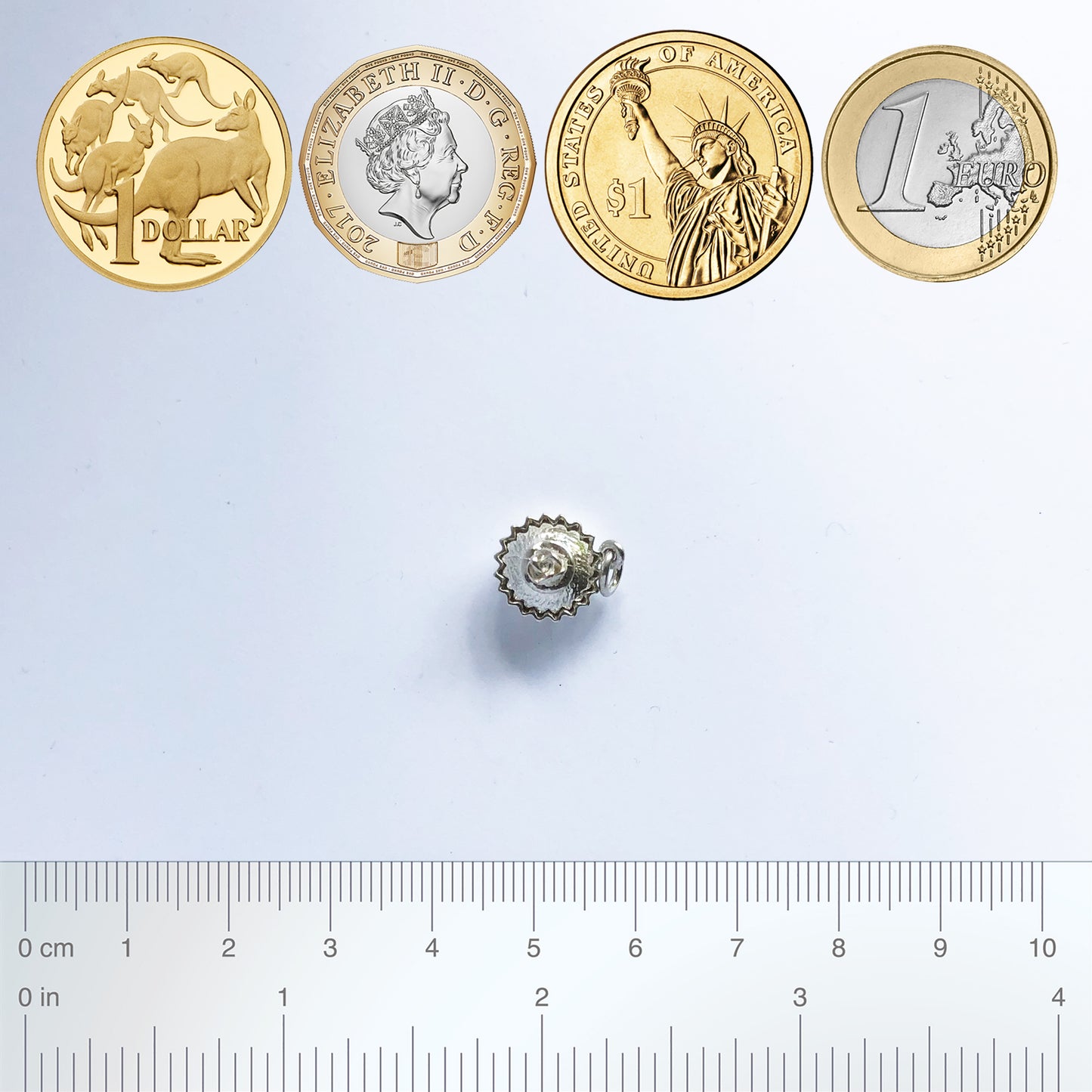 Sterling silver cupcake charm with coins and ruler for scale on a white background
