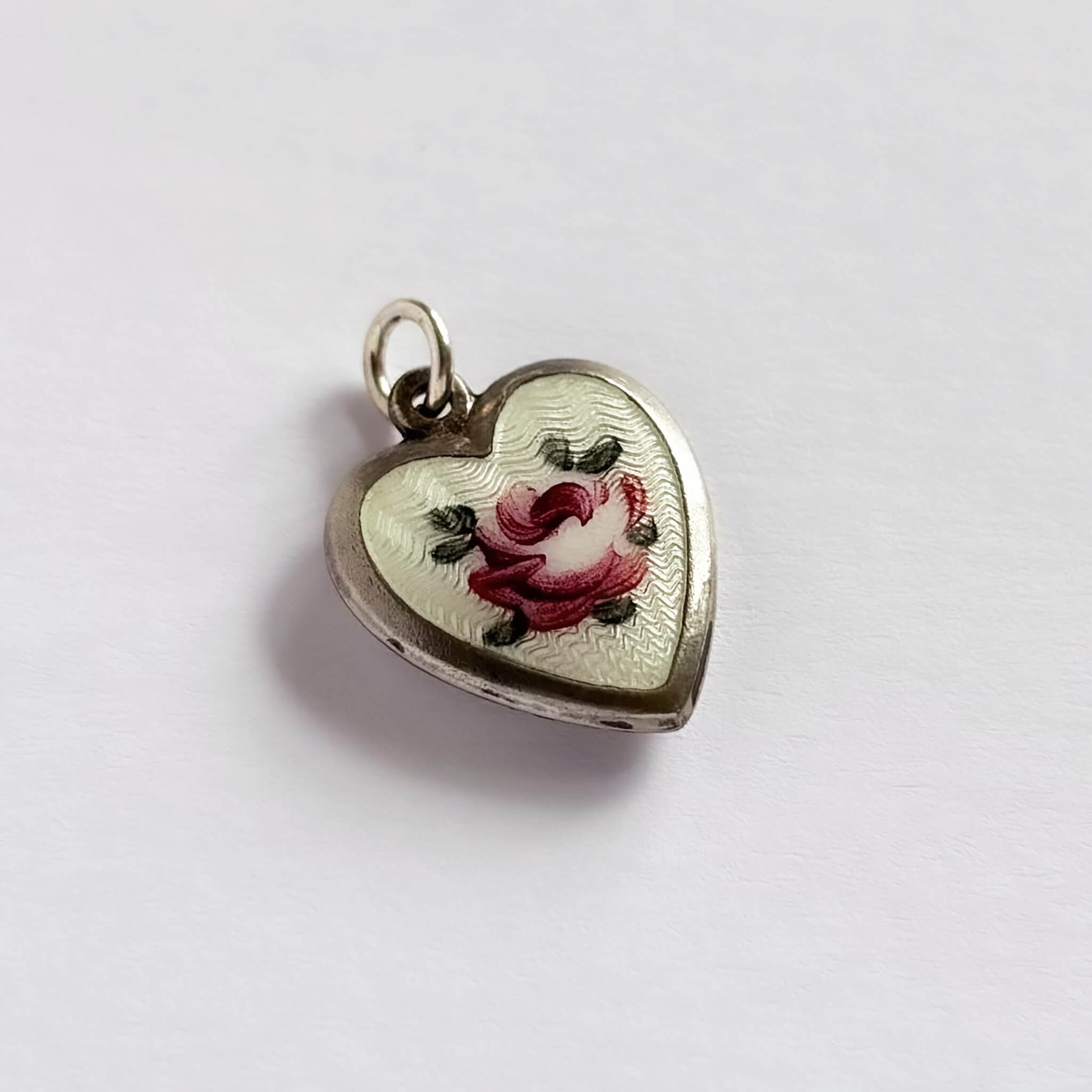 A 1940s sterling silver heart shaped charm with white guilloche enamel and a pink rose