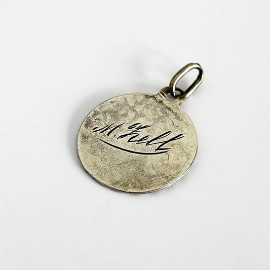Silver pendant with engraved text on a white background