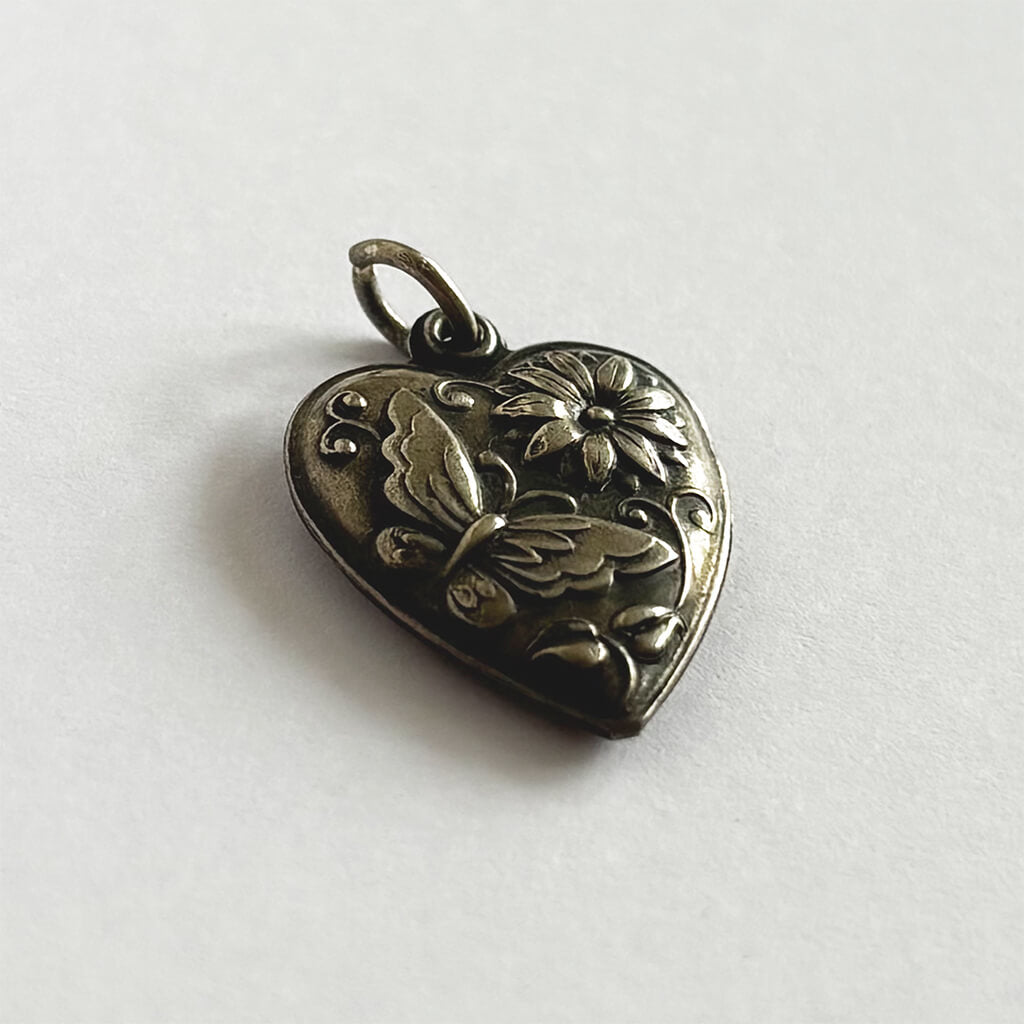 Heart-shaped silver charm with floral and butterfly design on a white background