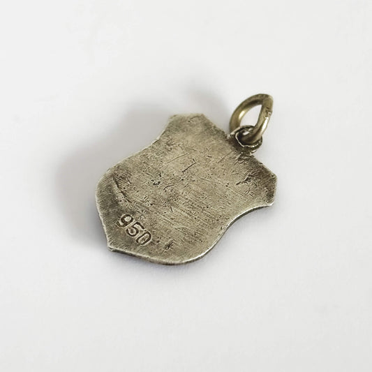 Back of a silver vintage travel shield charm on a light grey background.