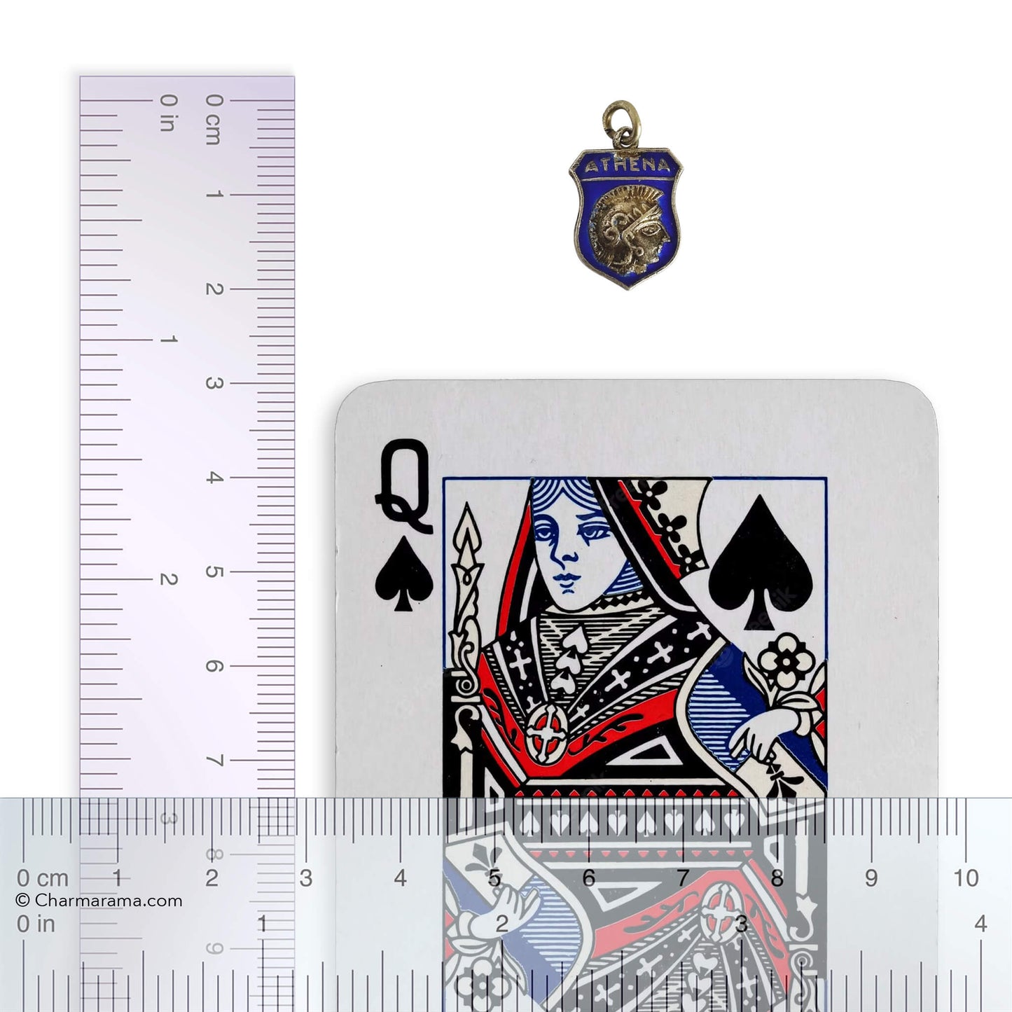 A vintage travel shield charm picturing the side view head of Goddess Athena on blue enamel with playing card and ruler for scale on white background.