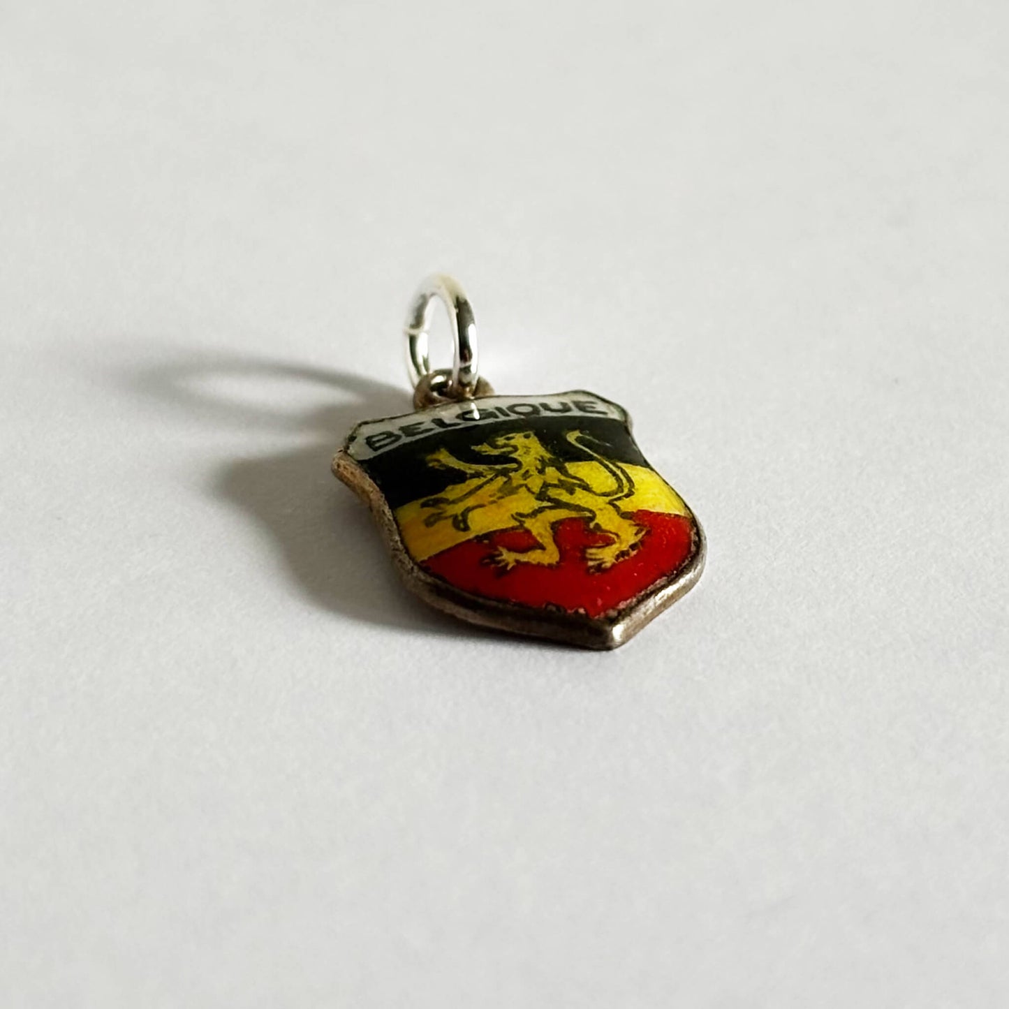 Vintage Belgium travel shield charm with black yellow and red enamel and rampant lion on white background.