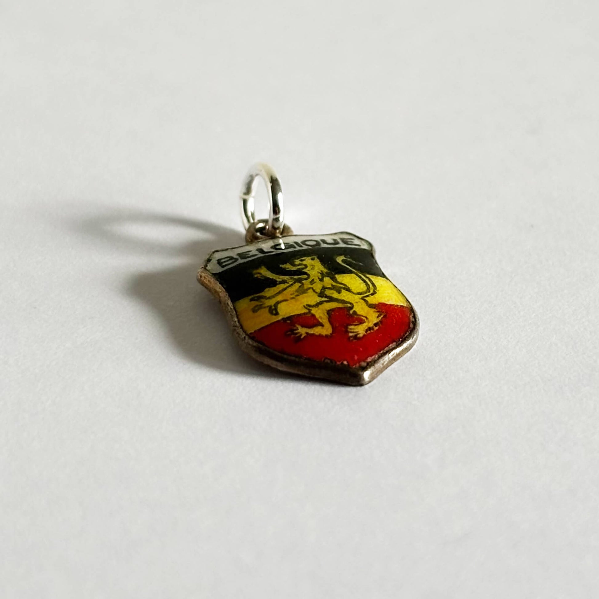 Vintage Belgium travel shield charm with black yellow and red enamel and rampant lion on white background.