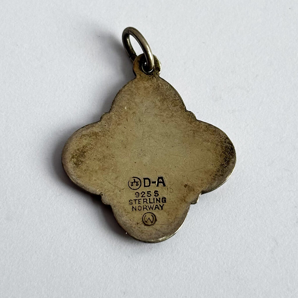 Quatrefoil-shaped silver pendant with 'D-A' and '925 S Sterling Norway' text on a light gray background