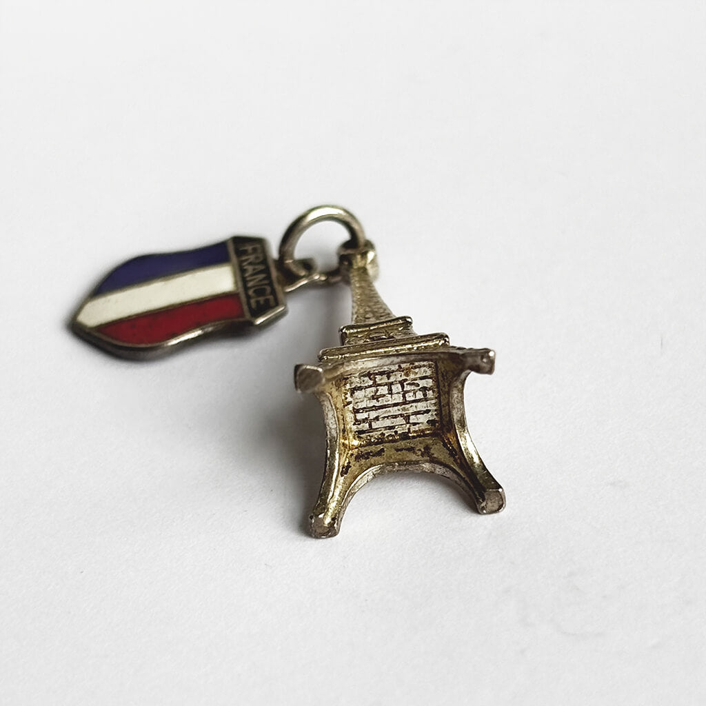 Two charms on a white background: one silver Eiffel Tower and the other with French flag design.