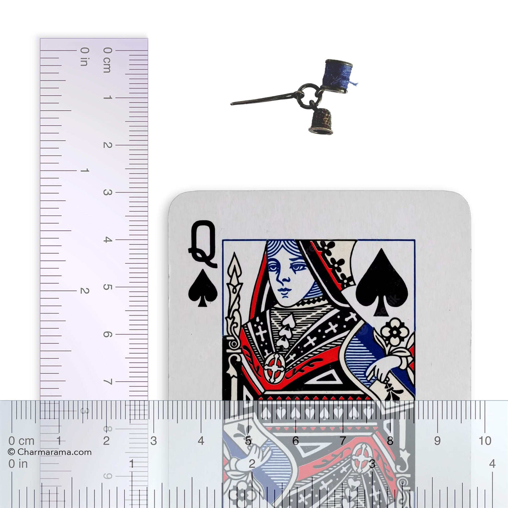 Sterling silver thimble needle and cotton reel charm with playing card and ruler for scale on a white background