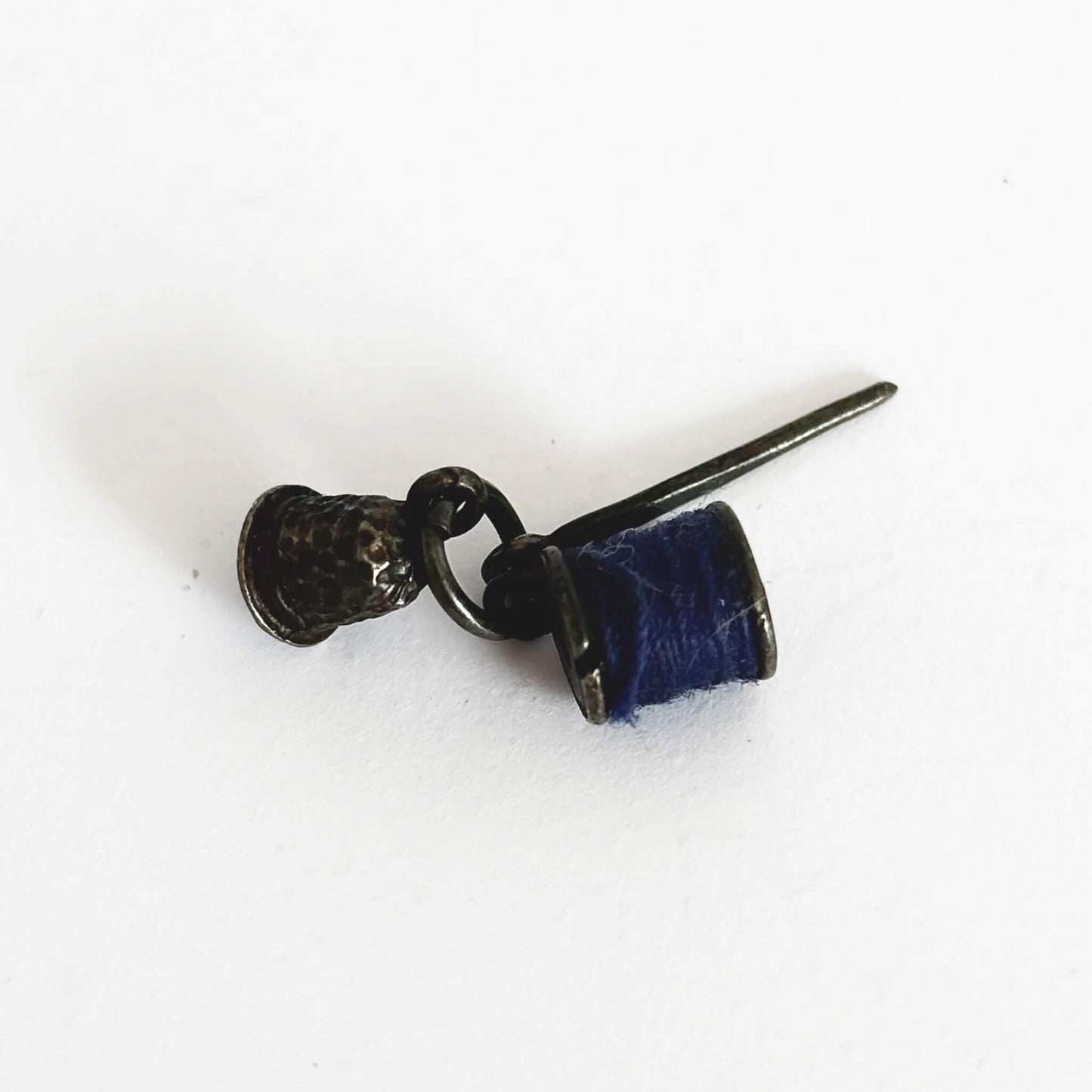Sterling silver thimble needle and cotton reel charm on a white background
