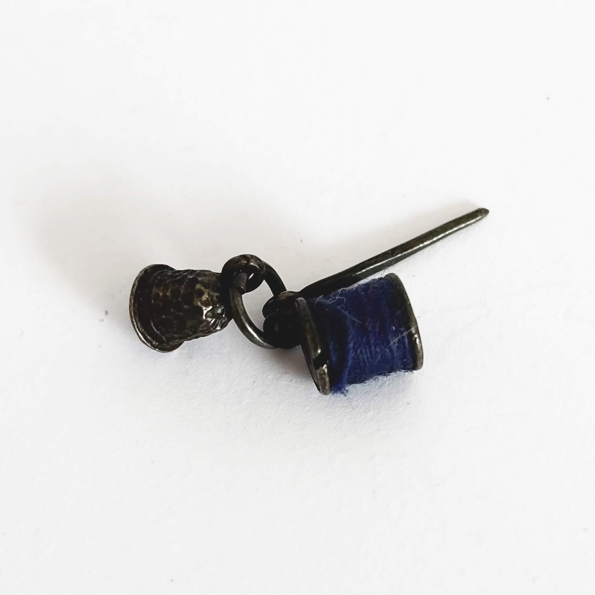 Sterling silver thimble needle and cotton reel charm on a white background