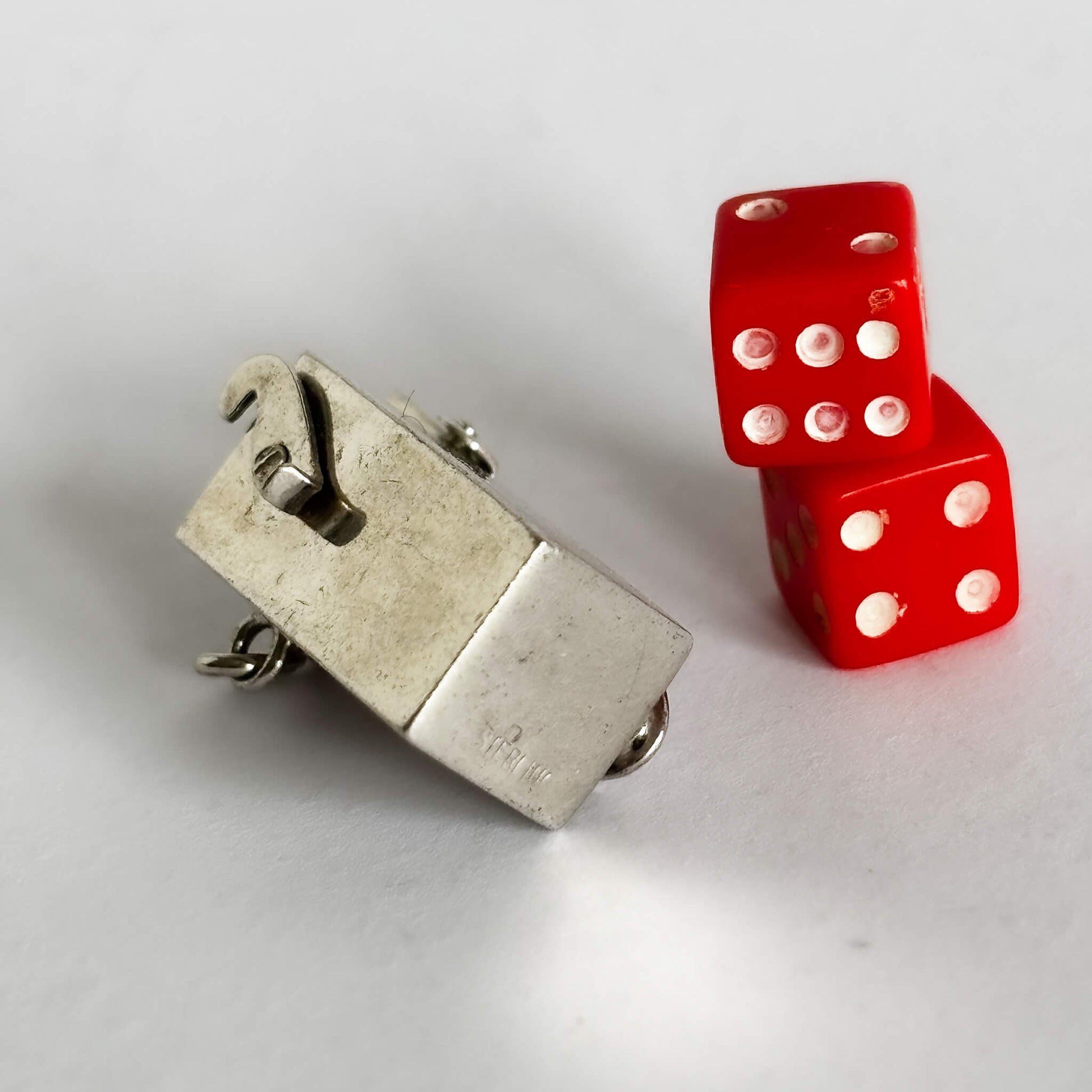 Two red dice with sterling silver box charm on a light grey background