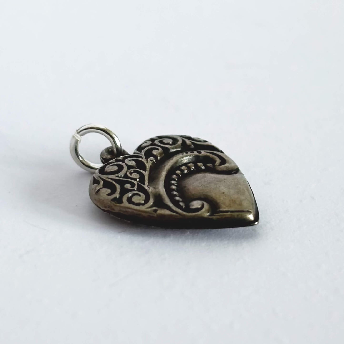 Silver heart-shaped pendant with intricate designs on a white background