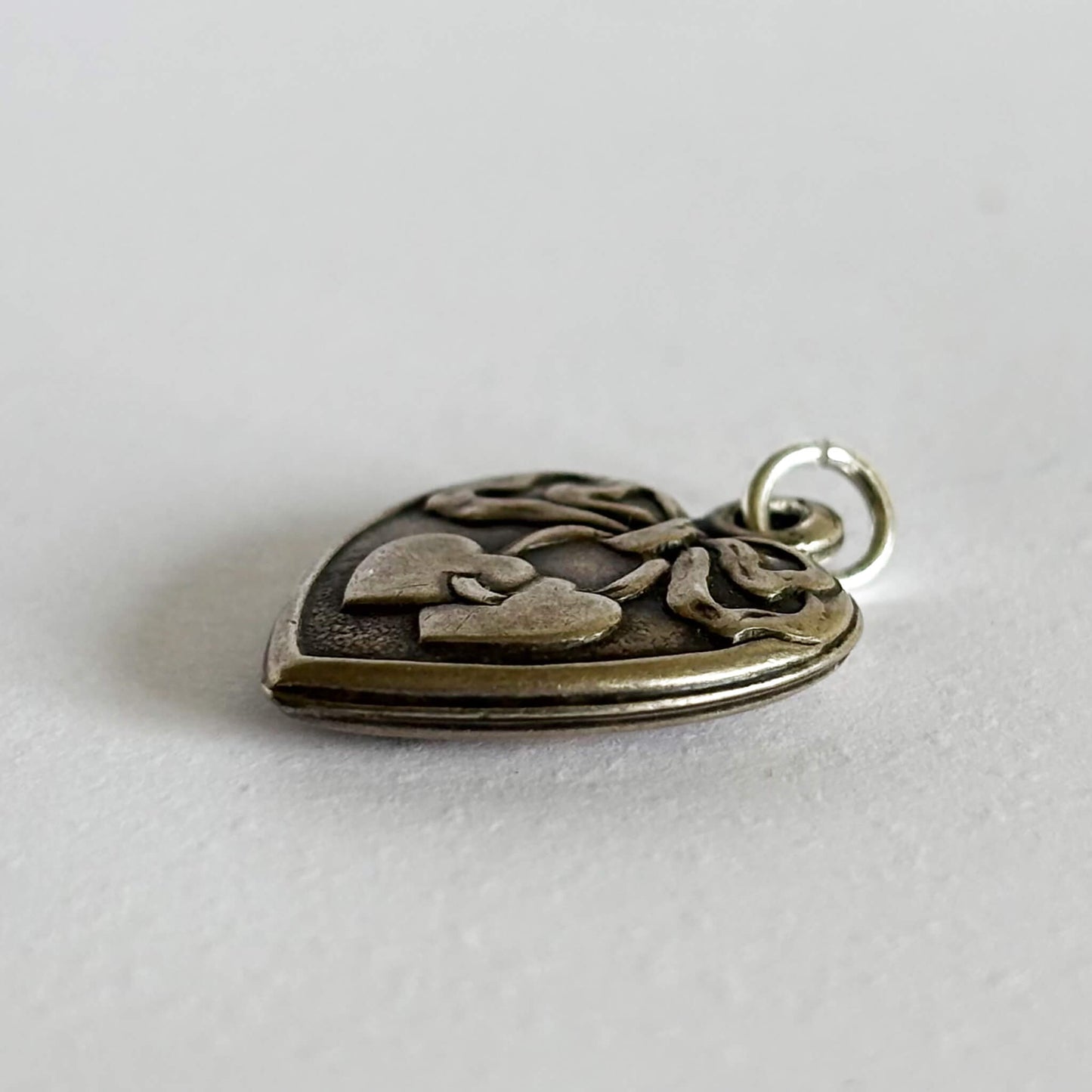 Silver heart-shaped pendant with heart and ribbon design on a light gray background