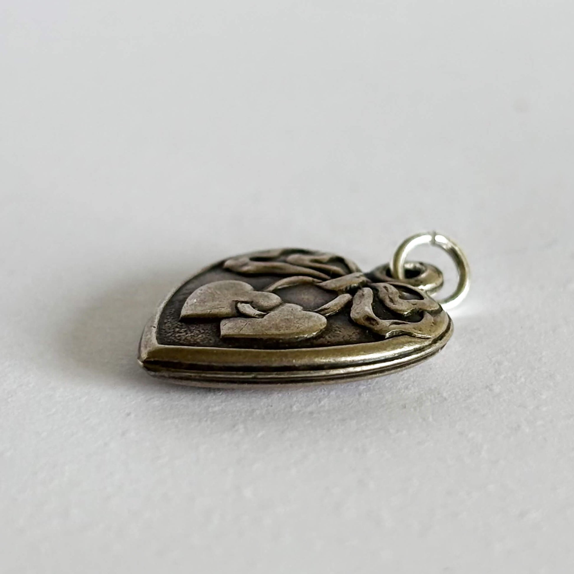 Silver heart-shaped pendant with heart and ribbon design on a light gray background