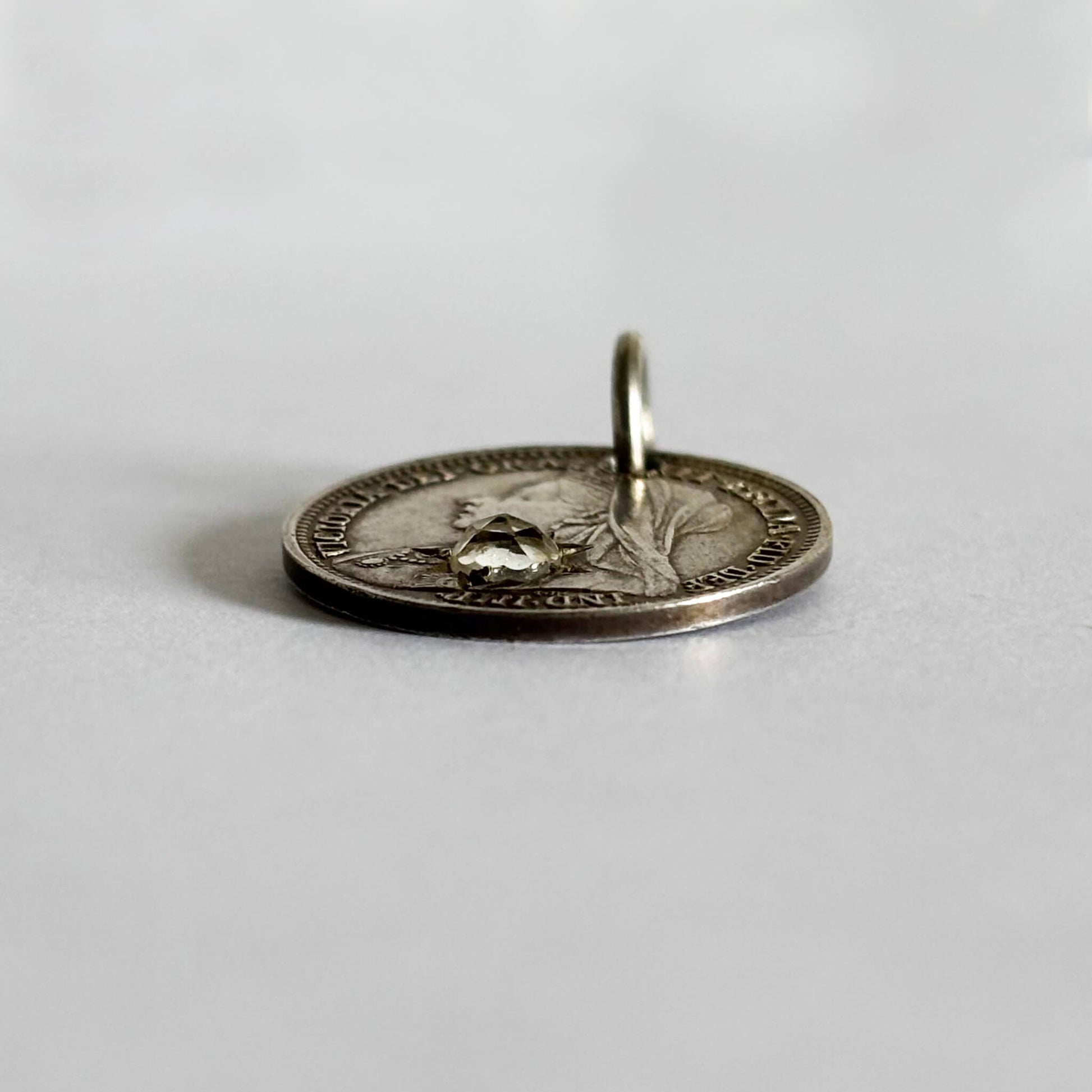 Silver coin pendant set with gem on a white background