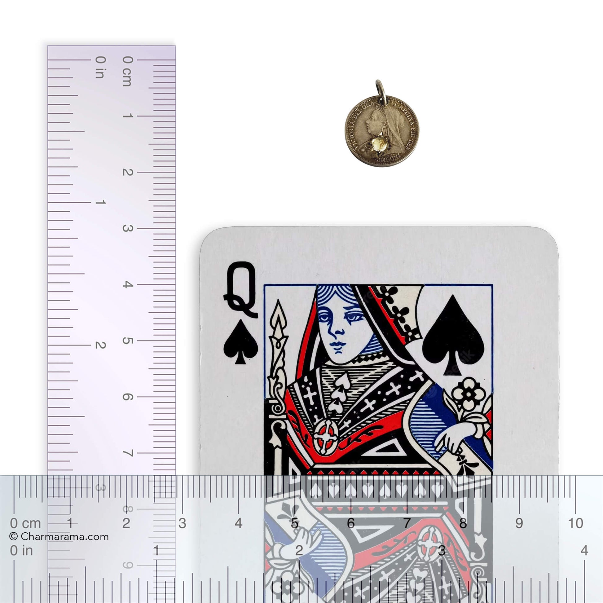 Victorian gem-set threepence with laying card next to a ruler for scale on a white background