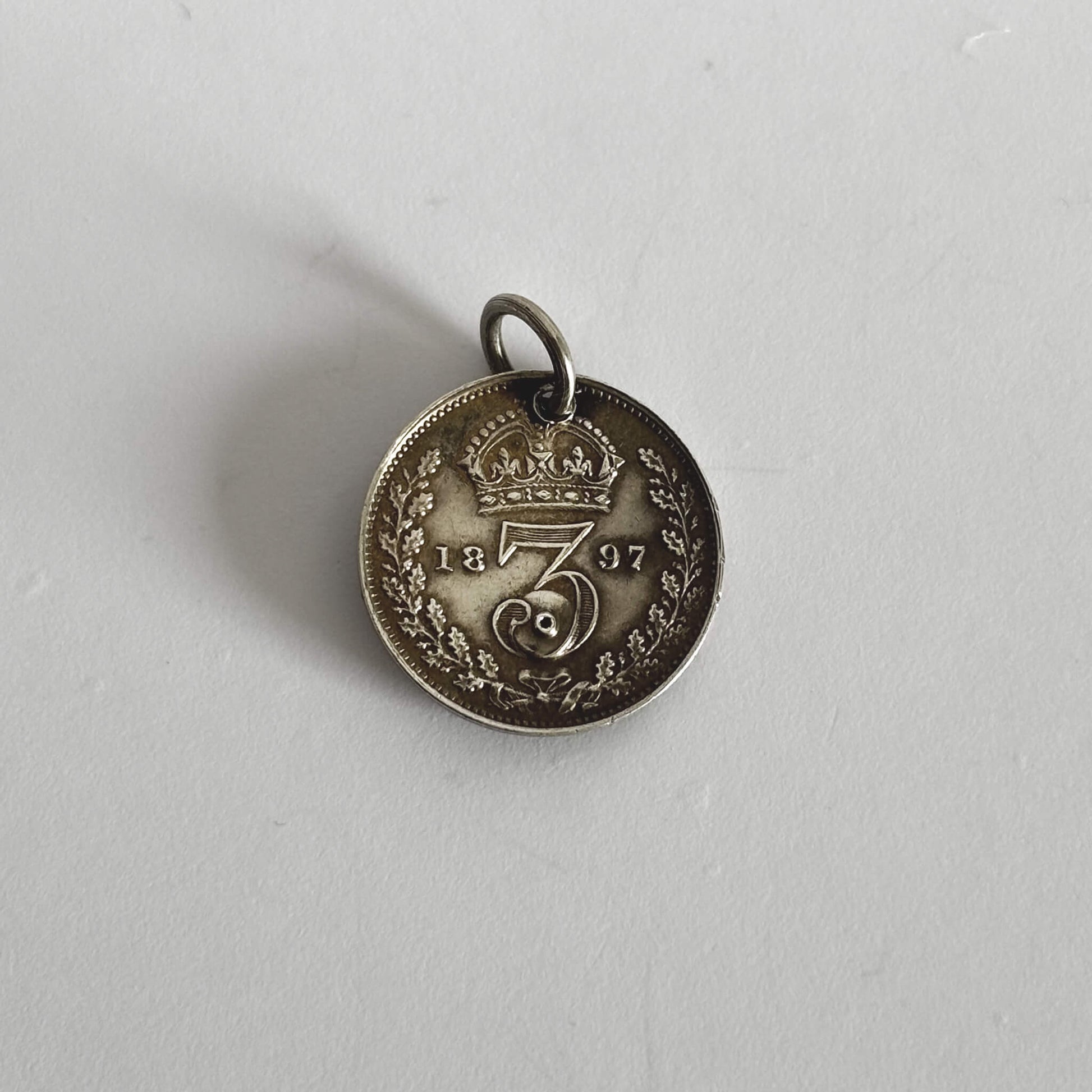 Silver coin pendant with '1897' on a light grey background