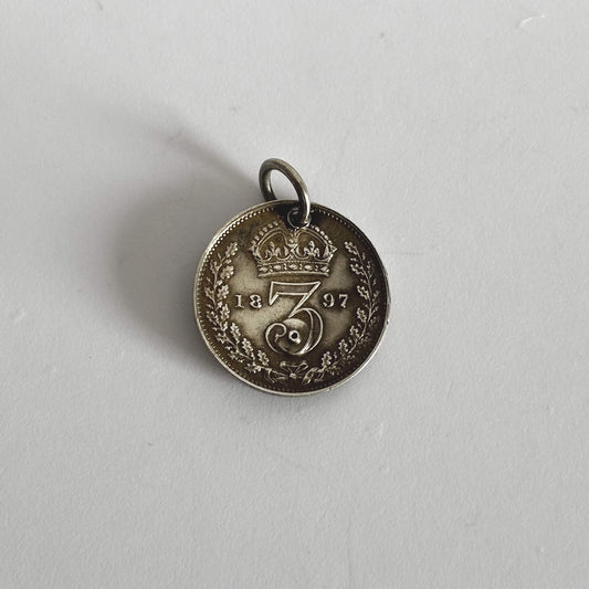 Silver coin pendant with '1897' on a light grey background