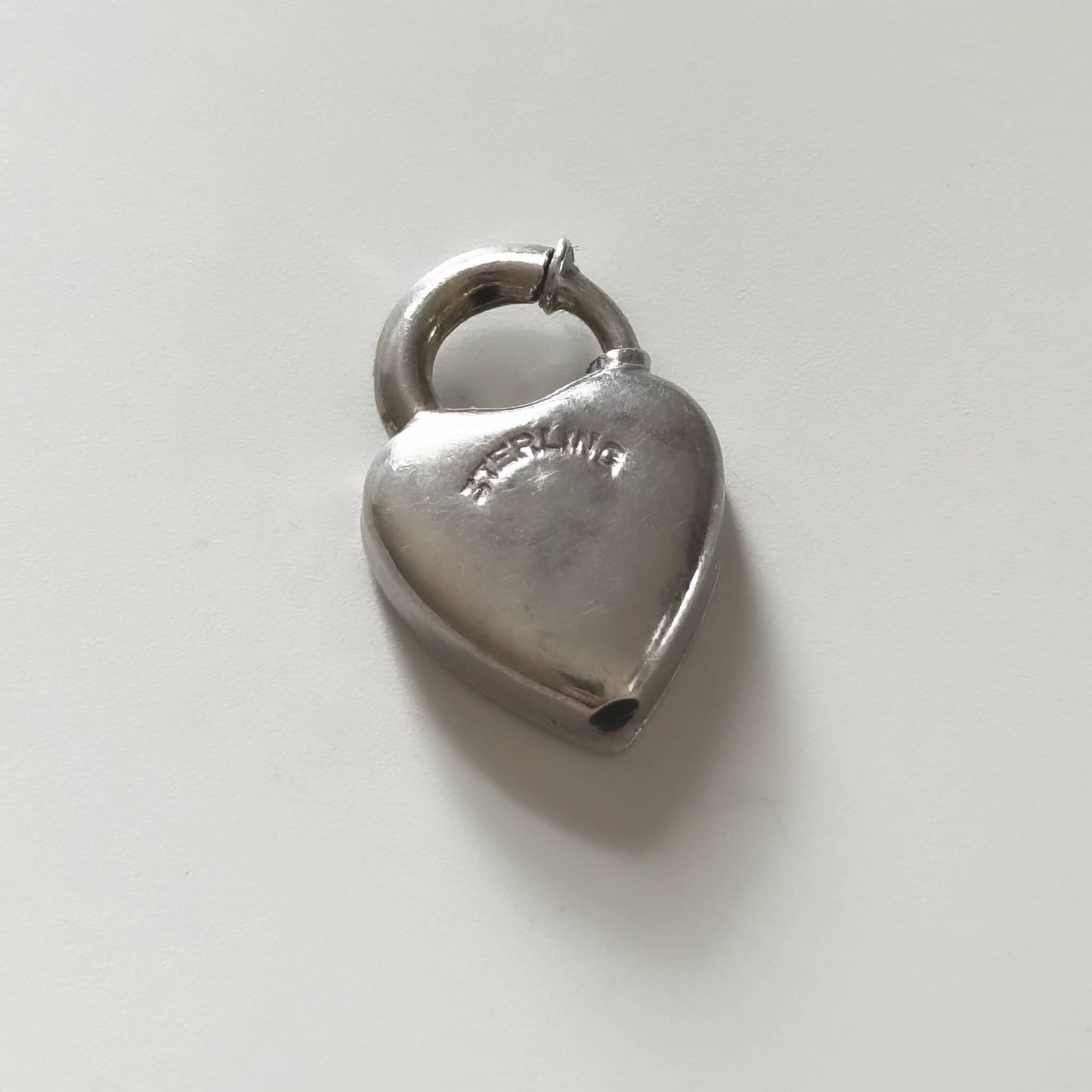 Silver heart-shaped padlock charm on a light gray background
