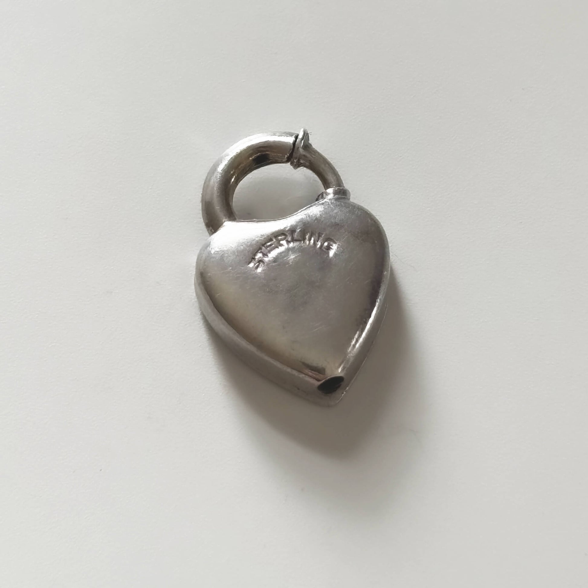 Silver heart-shaped padlock charm on a light gray background