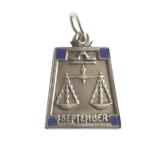 Silver trapezoid shape pendant with Libra zodiac sign and 'September' text with four dark blue enamel corner squares, on a white background