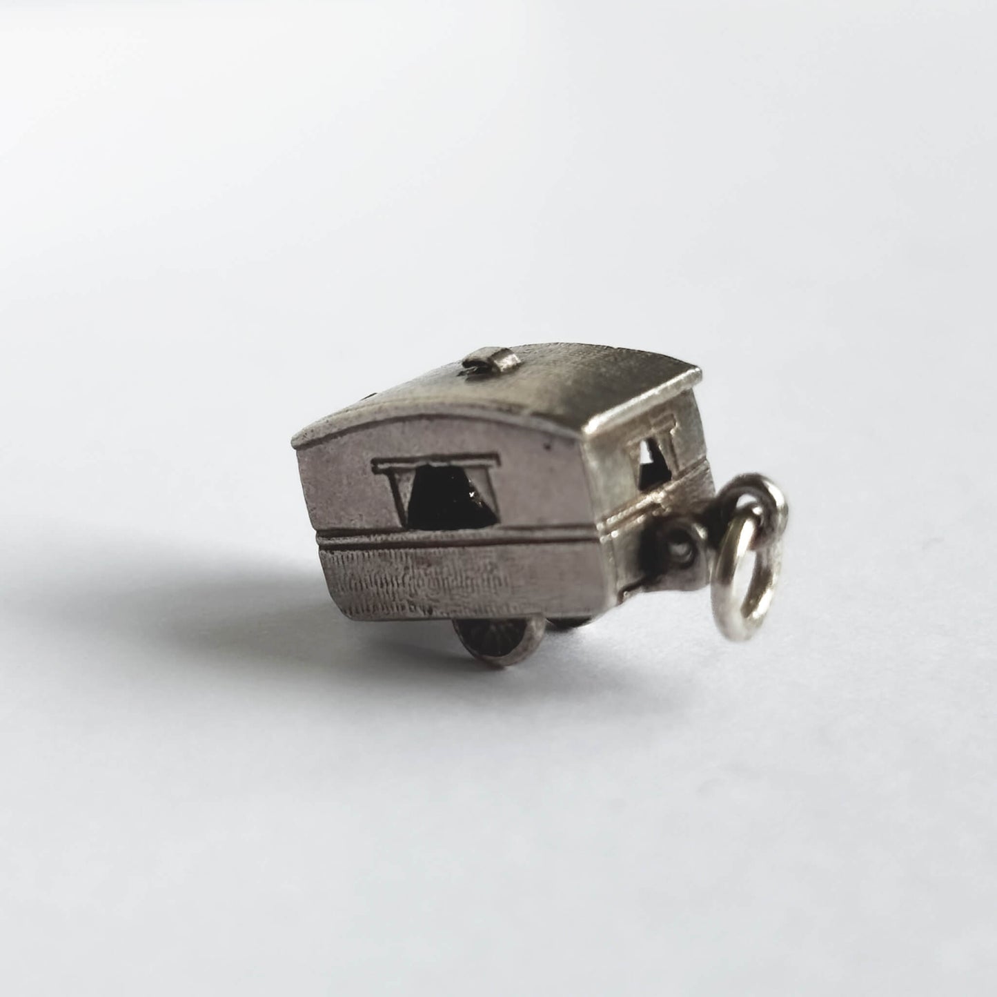 Vintage silver opening caravan charm on a white background.