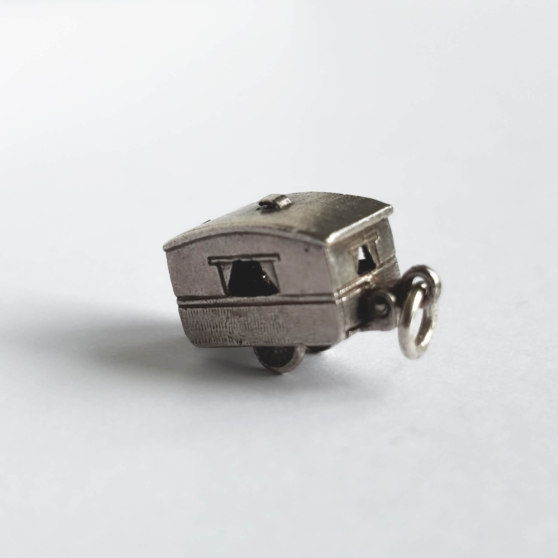 Vintage silver opening caravan charm on a white background.