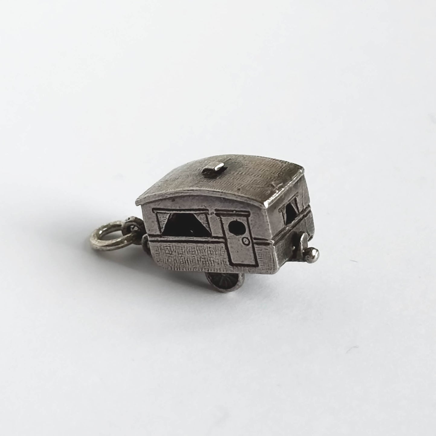 Vintage silver opening caravan charm on a white background.