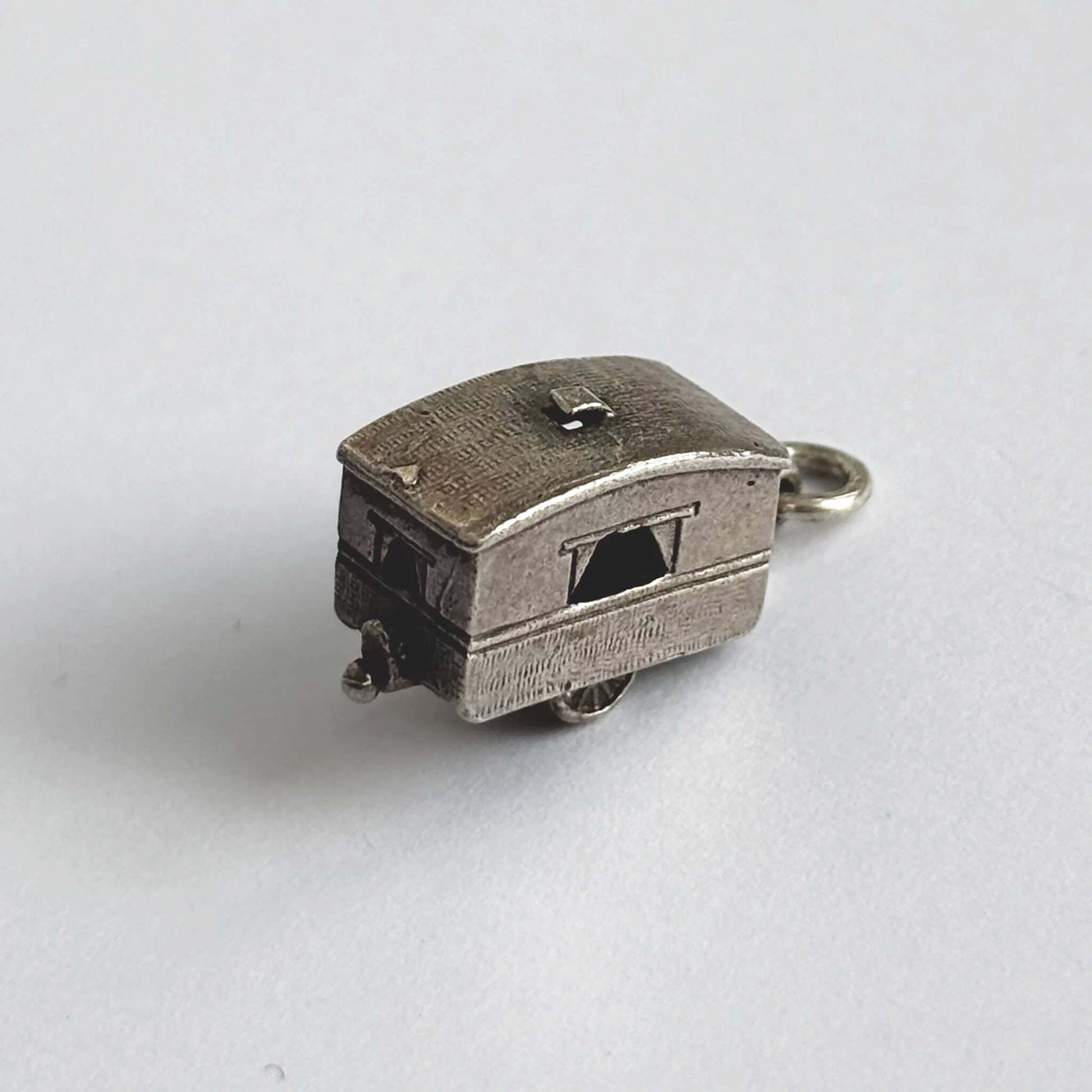 Vintage silver opening caravan charm on a white background.