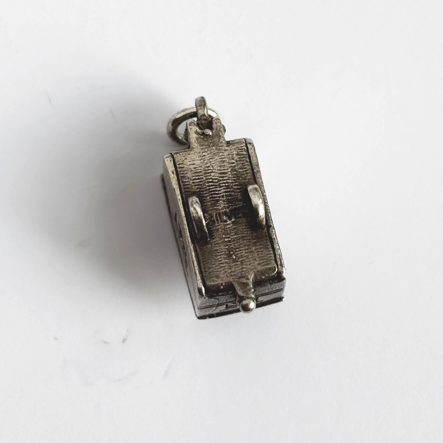 Underneath of vintage silver opening caravan charm on a white background.