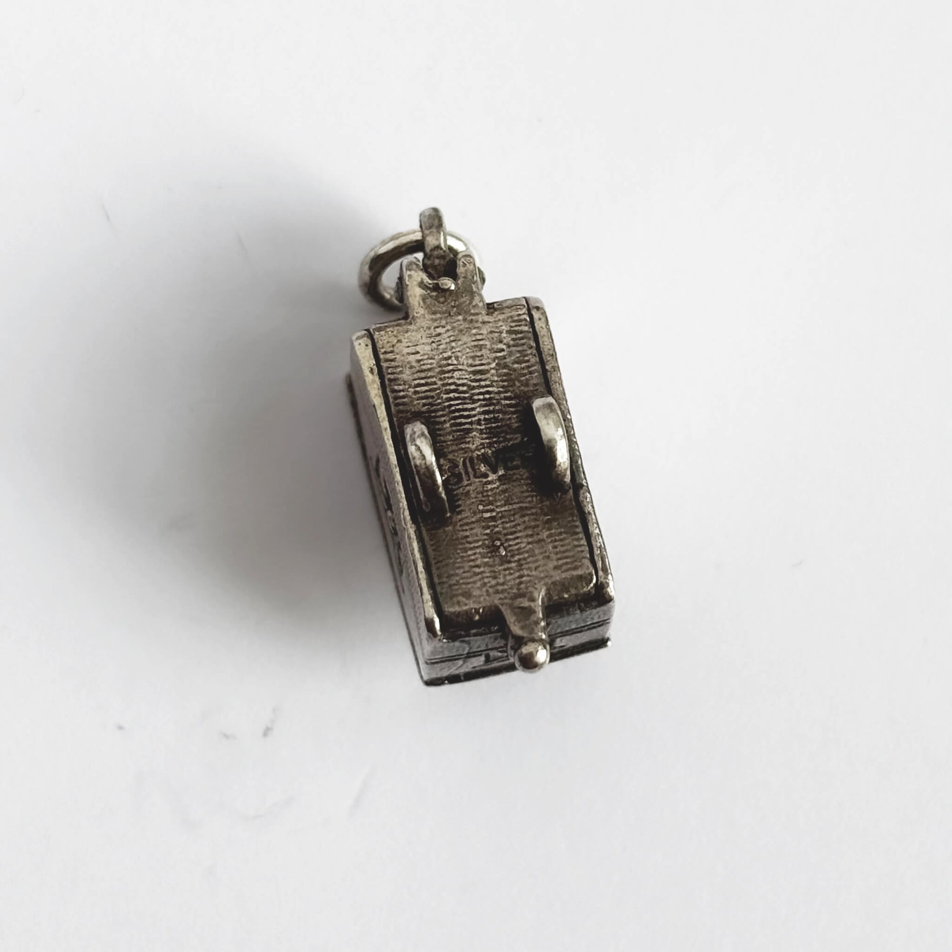 Underneath of vintage silver opening caravan charm on a white background.