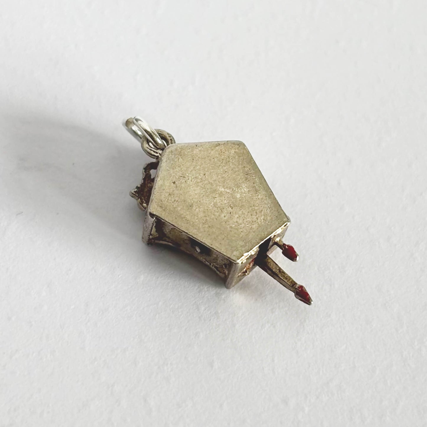 Small silver cuckoo clock charm viewed from back on a white background