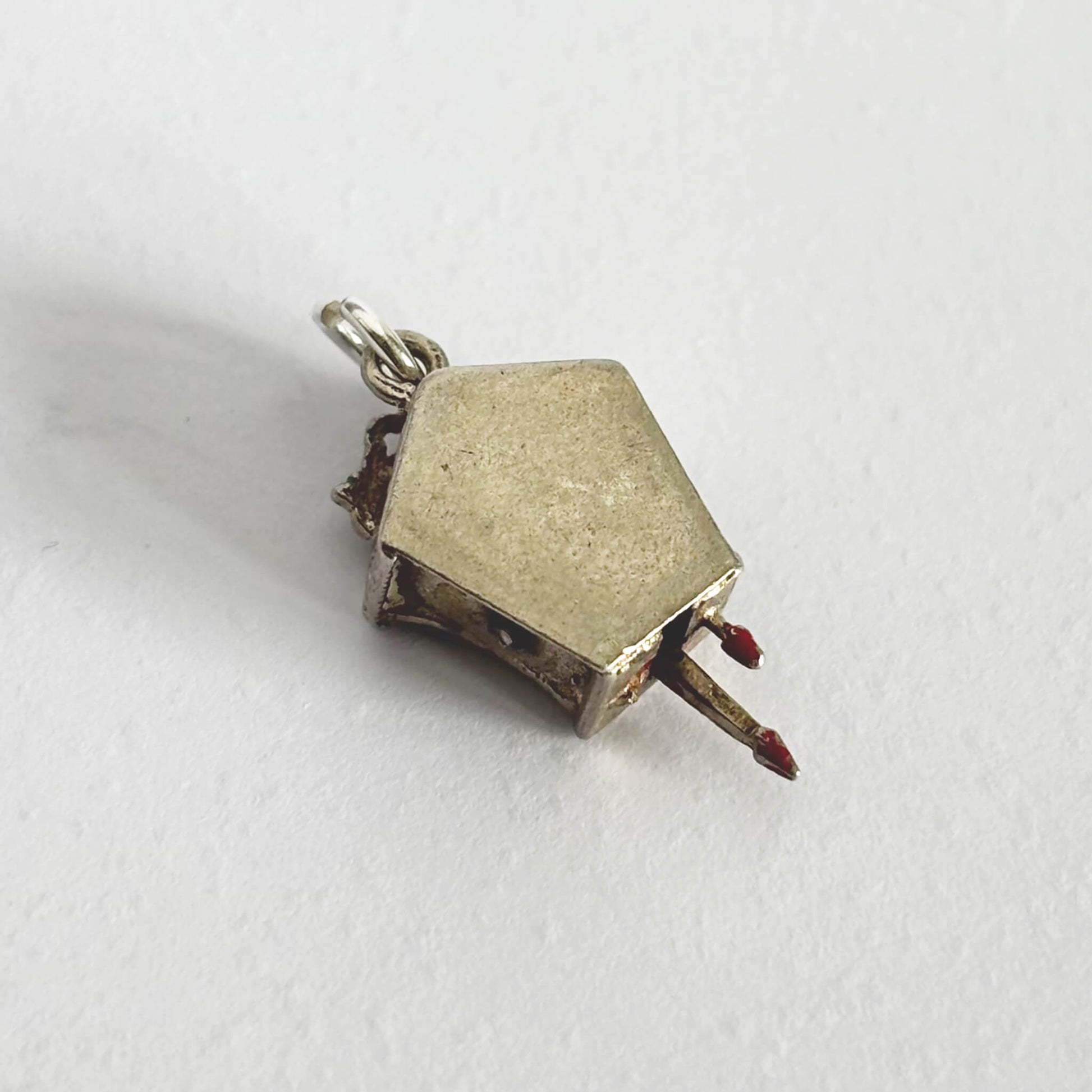 Small silver cuckoo clock charm viewed from back on a white background