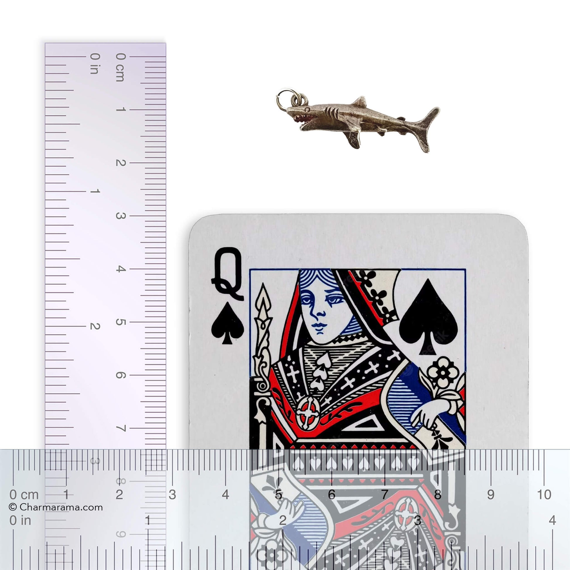 silver shark charm with laying card and ruler for scale on a white background