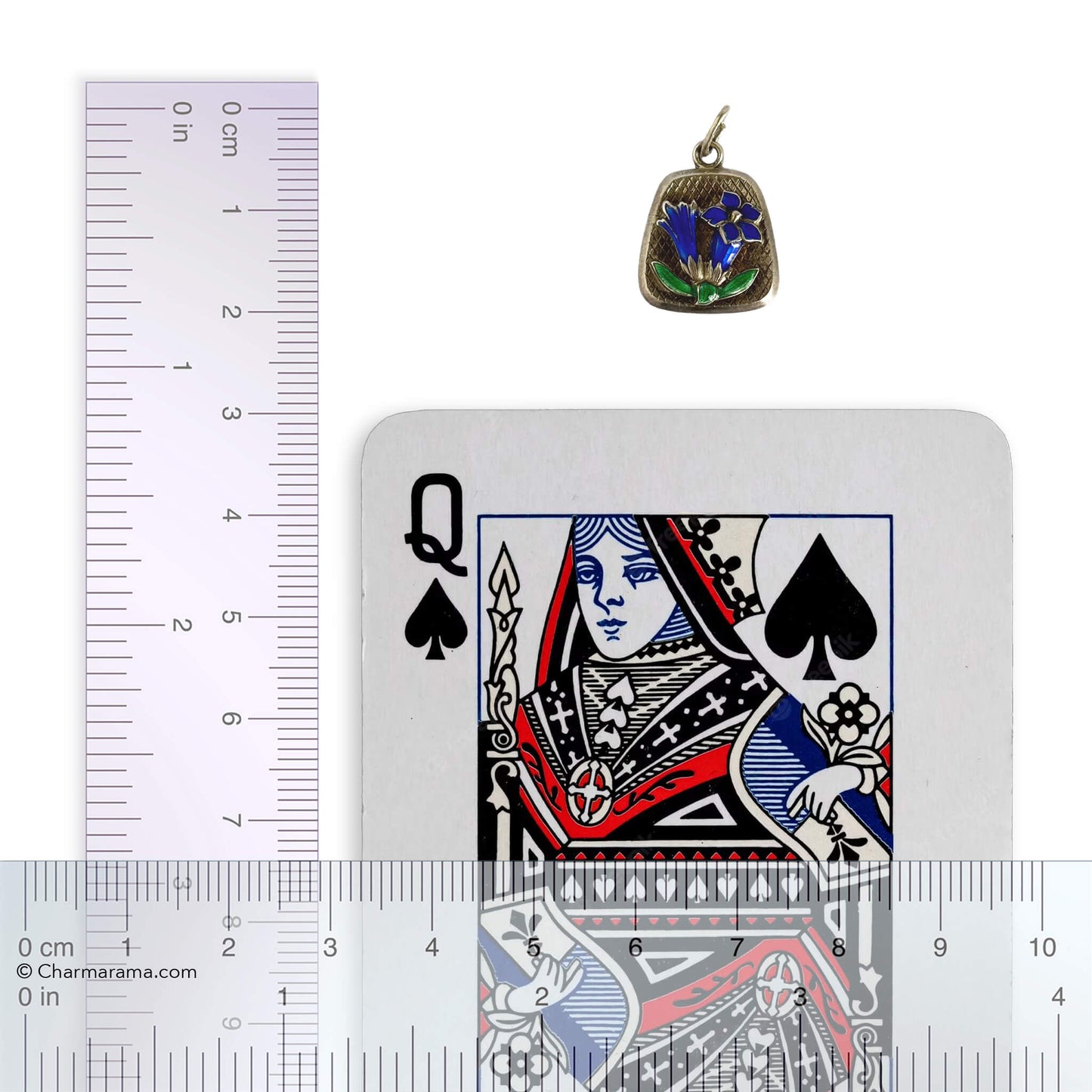 Vintage silver and enamel floral charm next to a playing card with a ruler for scale