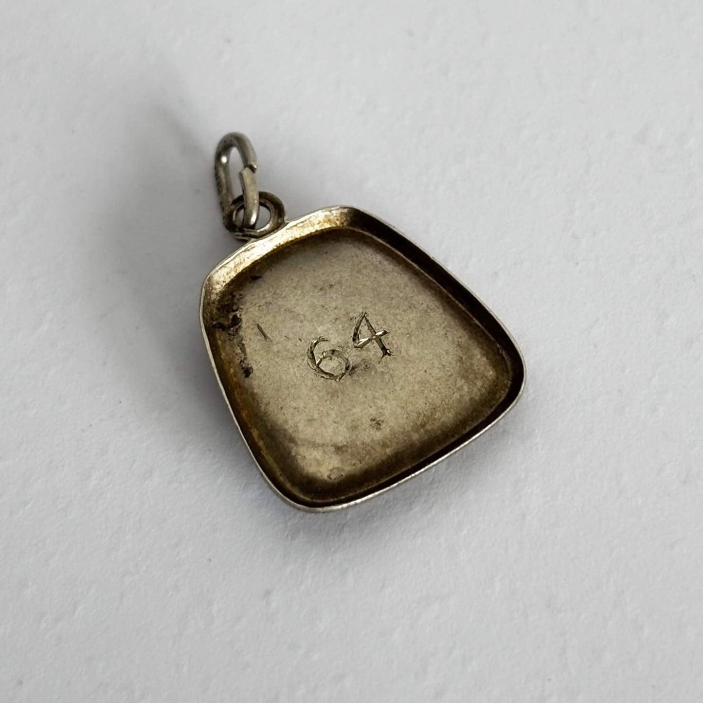 Silver pendant with '64' engraved on a light gray background
